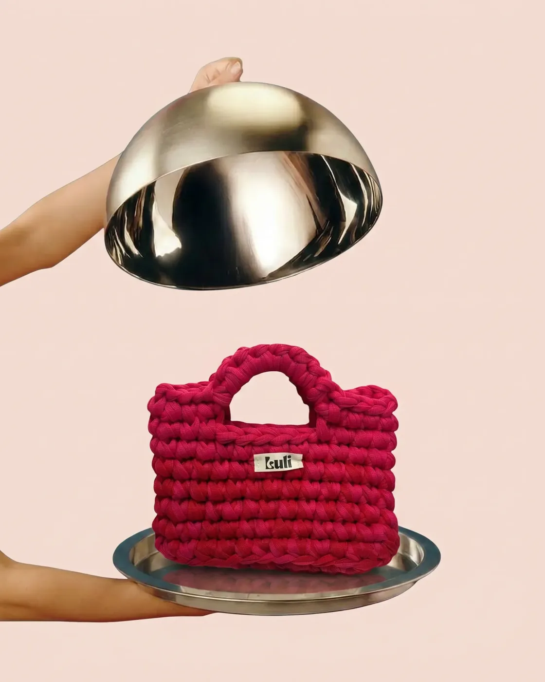 Bolsa de crochê vermelha revelada sob uma cloche prateada